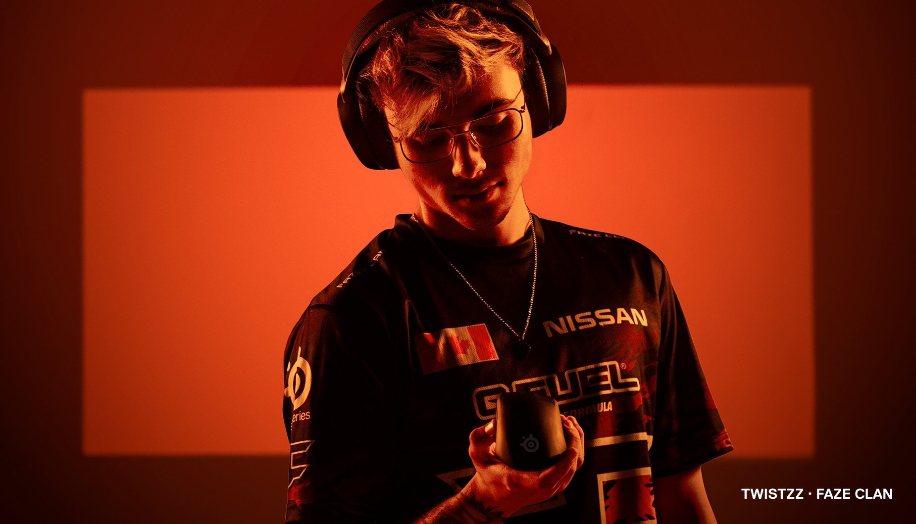 
 Faze Clan player Twistzz stands against an orange background holding the Prime mouse.
 