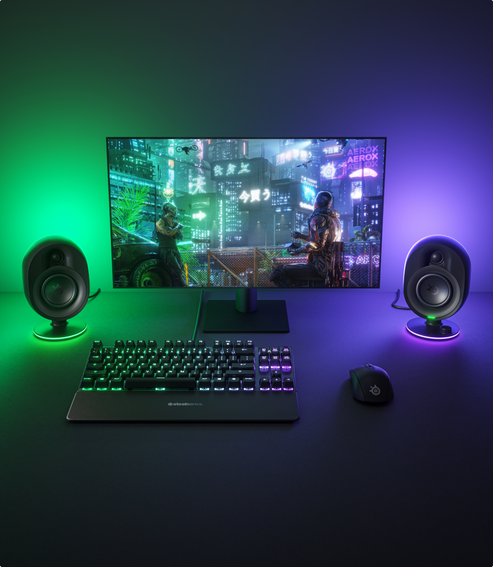 A desktop setup with Arena 7 speakers glowing with green and purple RGB.